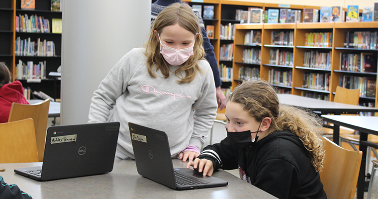 Two masked students on laptops