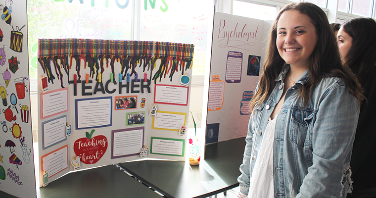 Student smiling with their project on "Teacher"