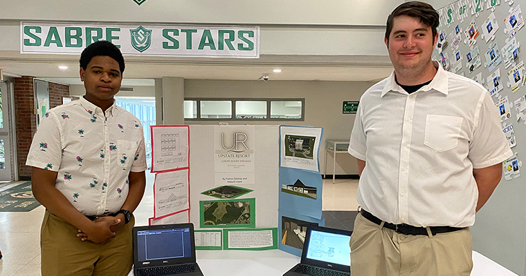 Two students standing in front of a poster that says "Upstate Resort"