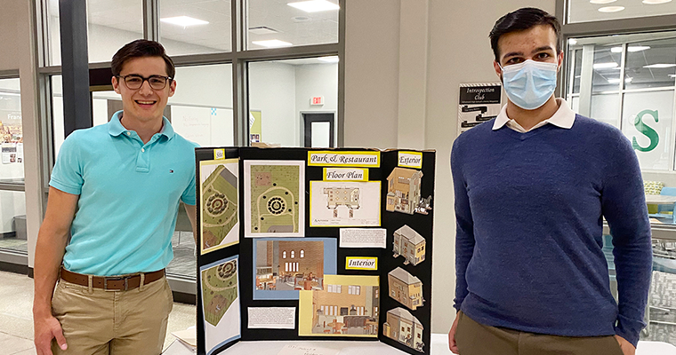 Two students standing in front of a poster that says "Park and Restaurant"