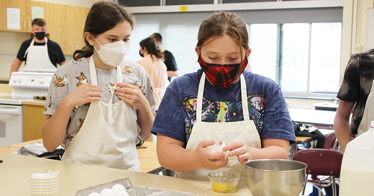 Student overlooking another student cracking an egg