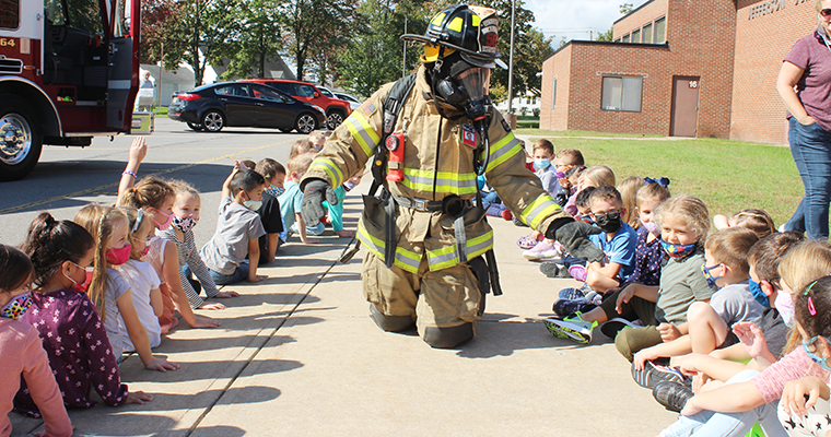 Firefighter kneeling, doing a demonstration for students