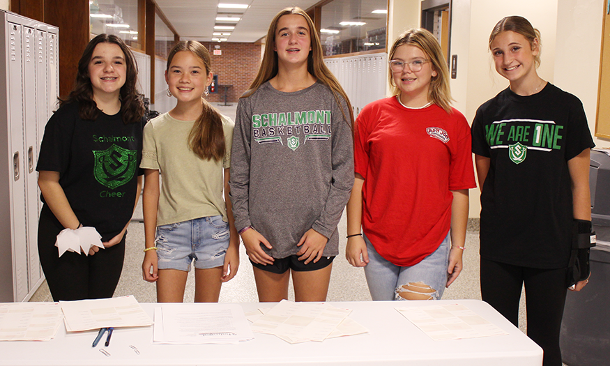 Students stand behind table