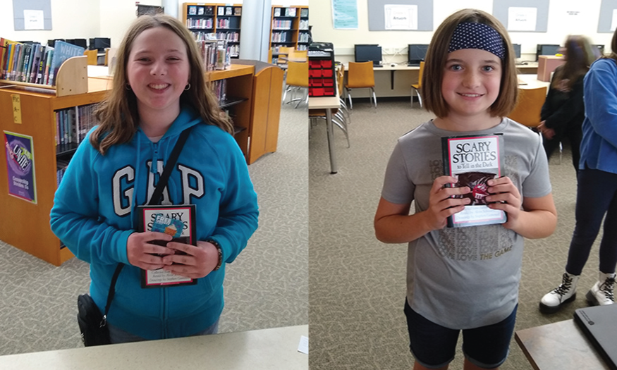 Two girls hold book in library