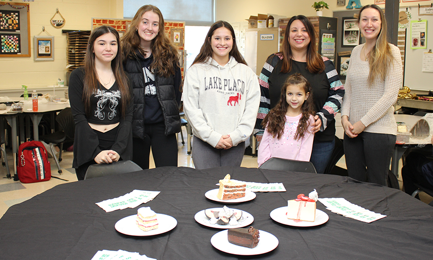Students and adults stand before table with dessert sculptures