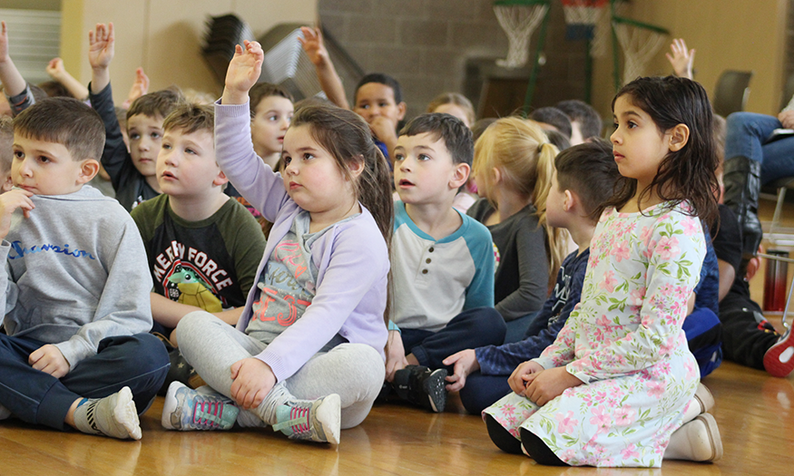 Students raise hand as assembly