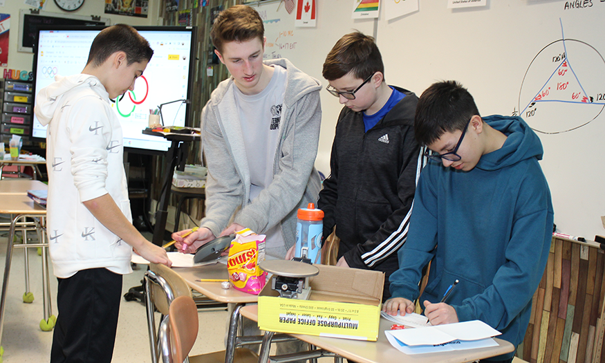 Students gather around desk for assignment