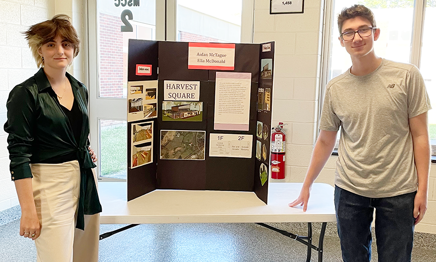 Students stand for photo in front of design plans