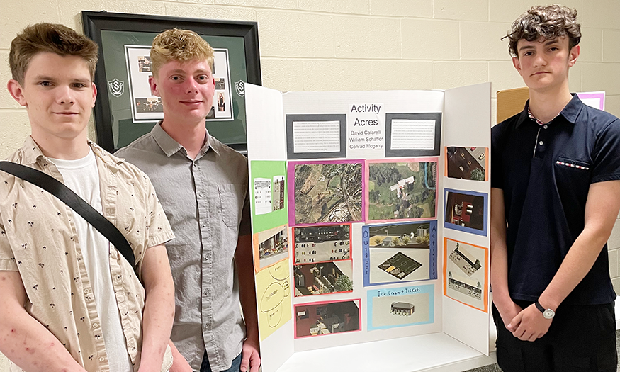 Students stand for photo in front of design plans