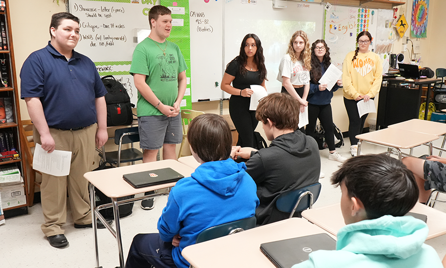 Students speak in front of a classroom